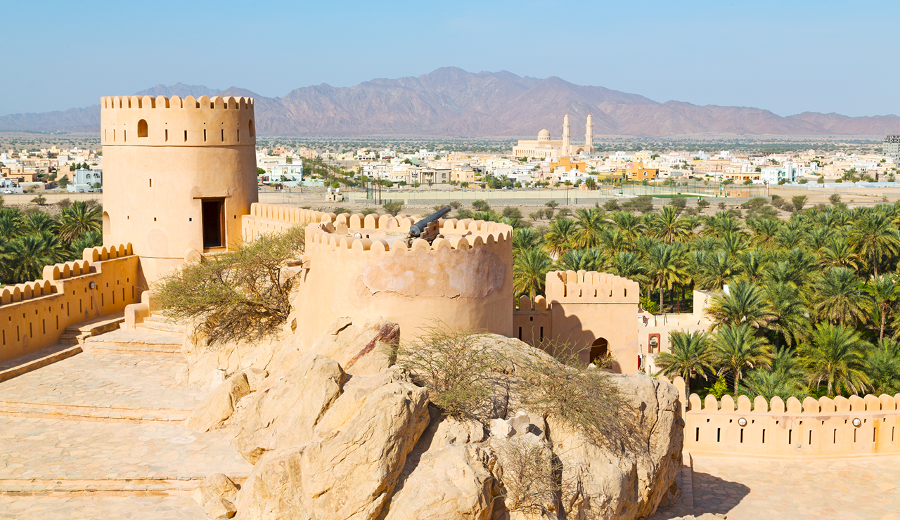 오만의 전통 요새와 사막 풍경 - 모래색 성벽과 탑이 있는 아랍 전통 건축물, 배경에 산맥이 보이는 중동의 역사적 유적